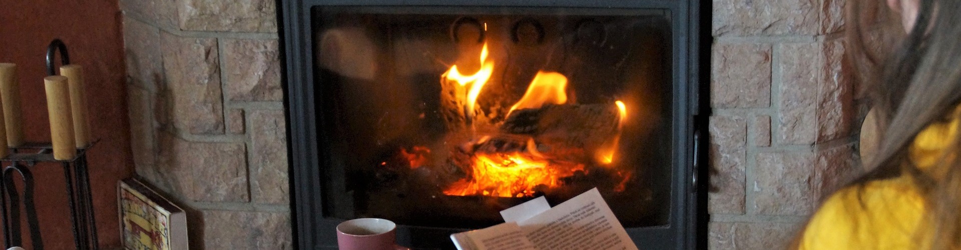 Frau sitzt vor einem Kamin mit einem Buch