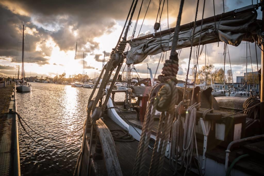 Robert Badorrek altes Holzschiff mit Segelbooten im Hintergrund und tollem Sonnenuntergang