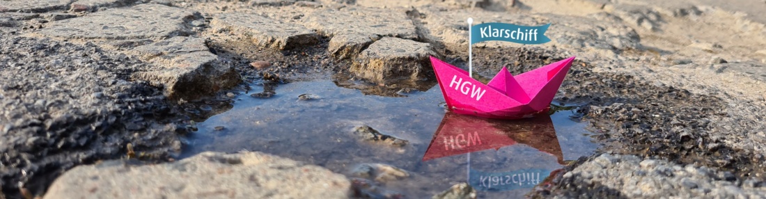 Klarschiff Banner © Franziska Vopel Auf dem Bild ist eine kaputte Straße. In einem Loch mit Wasser schwimmt ein Papierschiff, auf dessen Fahne steht Klarschiff geschrieben