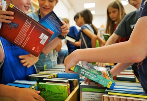 Mehrere Mädchen und Jungen schauen sich Bücher in einer hölzernen Bücherkiste an
