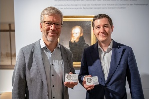 Dr Stefan Fassbinder und Lars Knevels von EuroMint zeigen die Jubiläumsmünze vor dem Porträt von Caspar David Friedrich im Pommerschen Landesmuseum